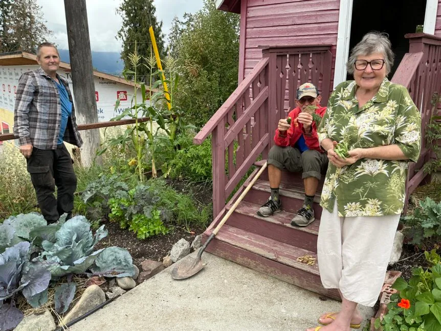 Volunteers stand outside the schoolhouse at the Creston Museum, holding vegetables they helped grow in the Victory Garden